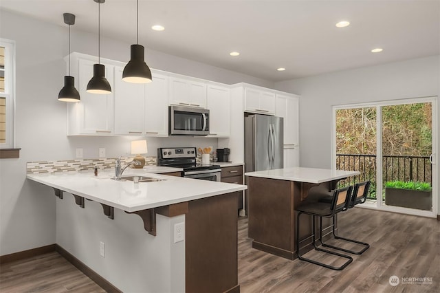 kitchen featuring a breakfast bar, decorative light fixtures, white cabinets, kitchen peninsula, and stainless steel appliances