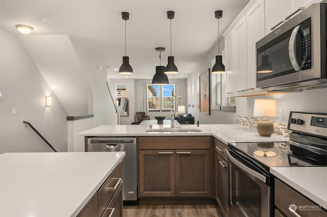 kitchen with sink, hanging light fixtures, kitchen peninsula, stainless steel appliances, and dark wood-type flooring