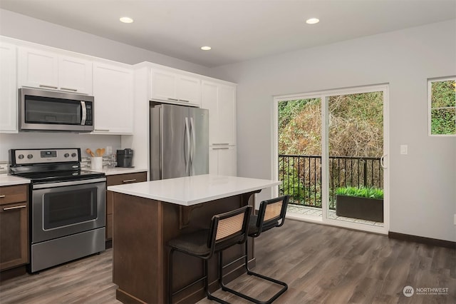 kitchen featuring a kitchen island, appliances with stainless steel finishes, white cabinets, a kitchen bar, and dark wood-type flooring