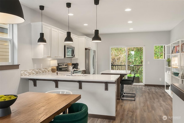 kitchen with pendant lighting, white cabinetry, stainless steel appliances, dark hardwood / wood-style floors, and a kitchen bar