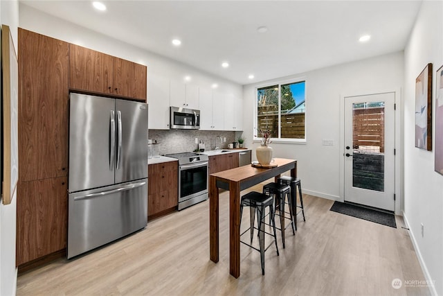 kitchen featuring white cabinetry, backsplash, light wood-type flooring, and appliances with stainless steel finishes