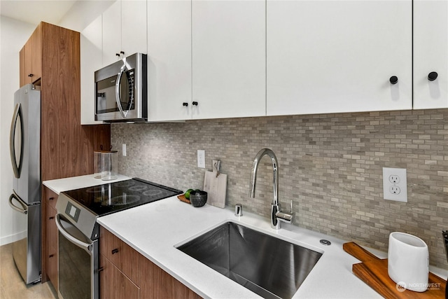 kitchen with white cabinetry, stainless steel appliances, sink, and backsplash