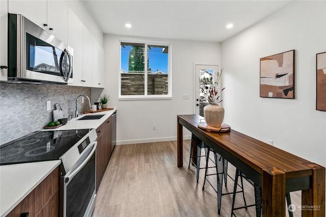 kitchen featuring appliances with stainless steel finishes, sink, white cabinets, backsplash, and light hardwood / wood-style floors