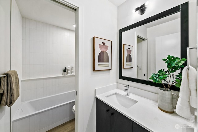 bathroom with tiled tub, vanity, hardwood / wood-style flooring, and toilet