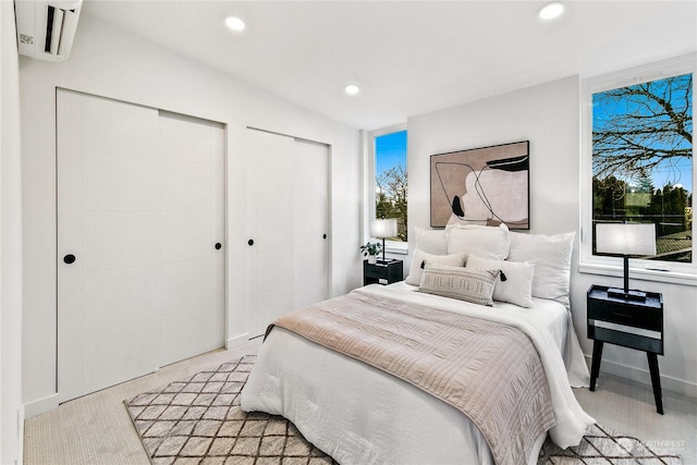 bedroom featuring two closets, light colored carpet, and an AC wall unit