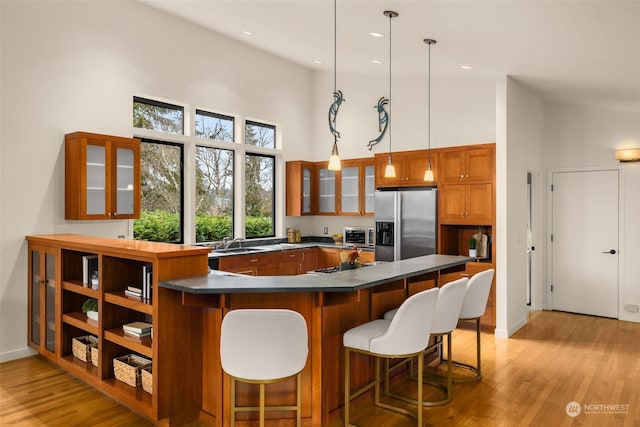 kitchen with a high ceiling, light hardwood / wood-style flooring, stainless steel fridge, and decorative light fixtures