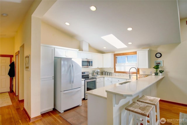 kitchen featuring a breakfast bar, stainless steel appliances, vaulted ceiling with skylight, a peninsula, and white cabinets