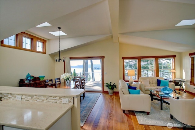 living room with high vaulted ceiling, a skylight, light wood-type flooring, and an inviting chandelier