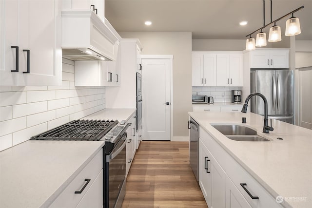 kitchen featuring sink, light hardwood / wood-style flooring, appliances with stainless steel finishes, white cabinets, and decorative light fixtures