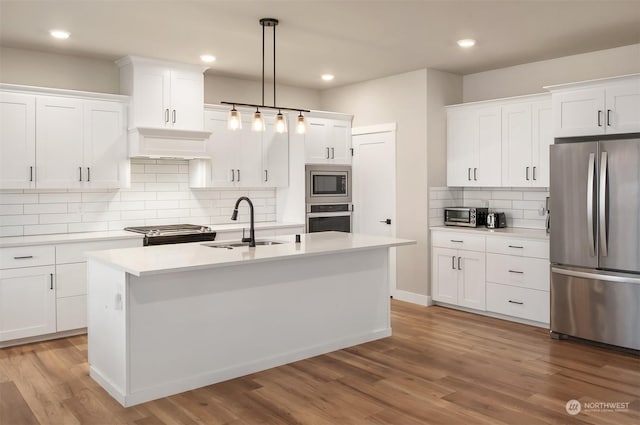 kitchen featuring sink, hanging light fixtures, an island with sink, stainless steel appliances, and white cabinets