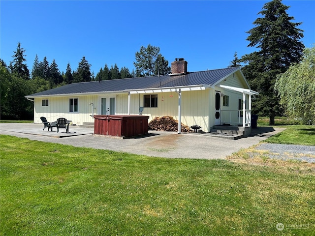 rear view of house with a hot tub, metal roof, a lawn, a chimney, and a patio