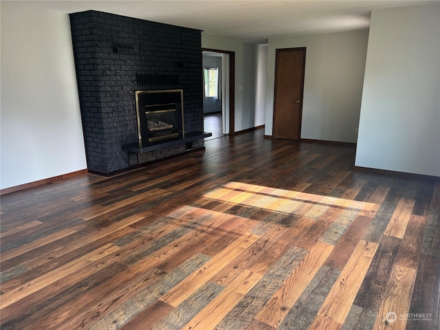 unfurnished living room featuring wood-type flooring, a brick fireplace, and baseboards