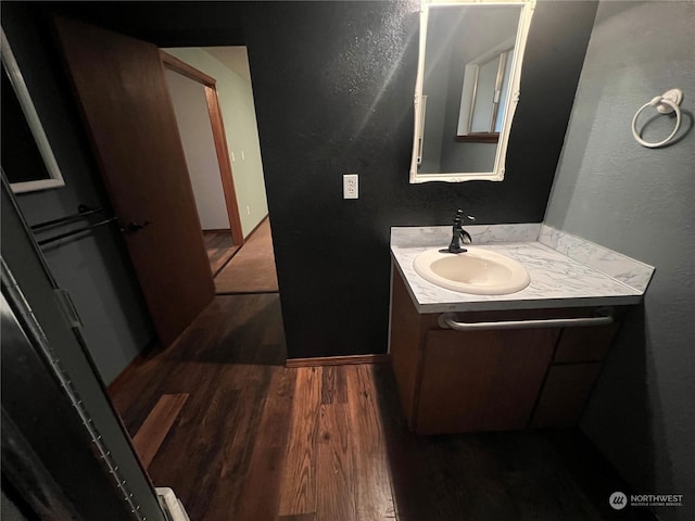 bathroom featuring a textured wall, baseboards, vanity, and wood finished floors