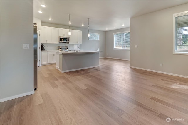 kitchen with white cabinetry, hanging light fixtures, an island with sink, stainless steel appliances, and light hardwood / wood-style floors