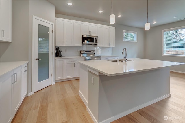 kitchen with a kitchen island with sink, sink, pendant lighting, and appliances with stainless steel finishes