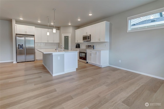 kitchen featuring white cabinetry, appliances with stainless steel finishes, a kitchen island with sink, pendant lighting, and light hardwood / wood-style floors