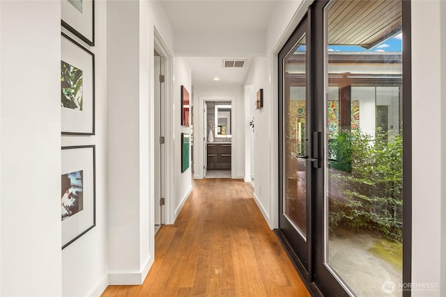 corridor featuring baseboards, light wood finished floors, and visible vents