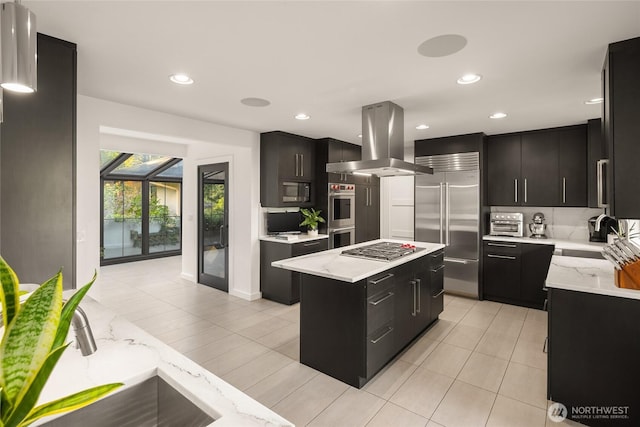 kitchen with a sink, a kitchen island, built in appliances, island range hood, and dark cabinets