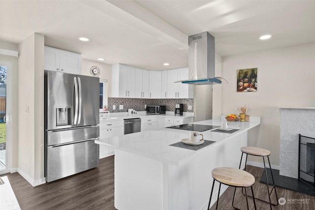 kitchen with a breakfast bar area, appliances with stainless steel finishes, white cabinets, island exhaust hood, and kitchen peninsula