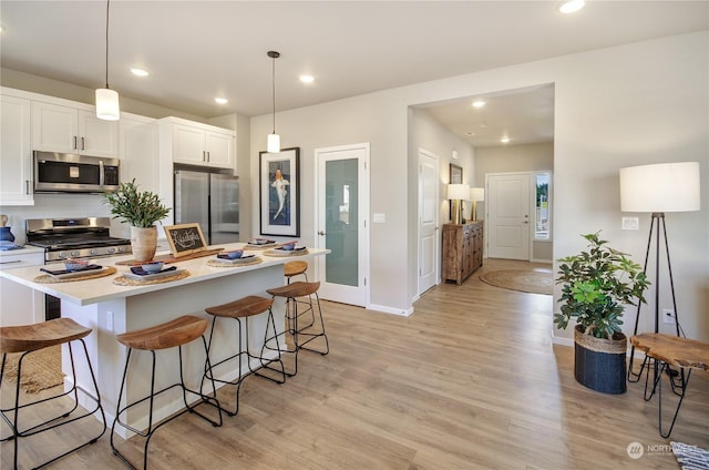 kitchen with white cabinetry, appliances with stainless steel finishes, a kitchen breakfast bar, and decorative light fixtures