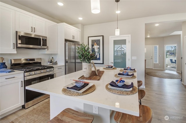 kitchen featuring a breakfast bar area, white cabinetry, appliances with stainless steel finishes, a kitchen island, and pendant lighting