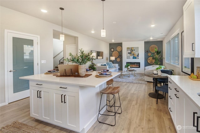 kitchen featuring hanging light fixtures, light wood-type flooring, a large fireplace, a kitchen breakfast bar, and white cabinets