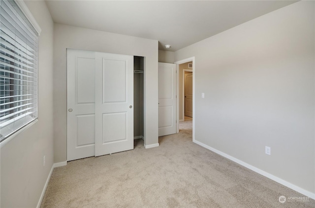 unfurnished bedroom with light colored carpet and a closet