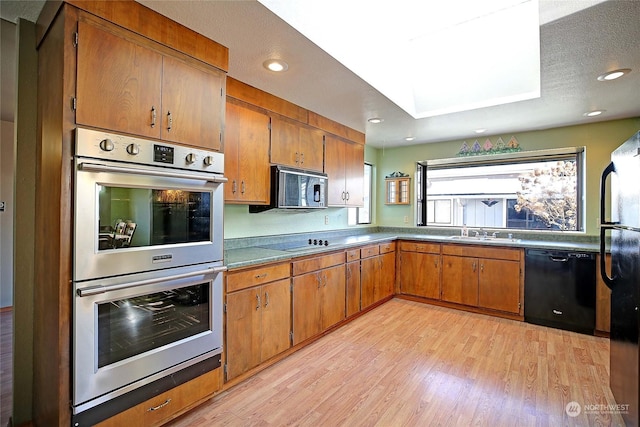 kitchen with sink, black appliances, a textured ceiling, and light wood-type flooring