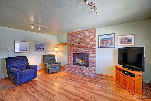 living room with rail lighting, a brick fireplace, light hardwood / wood-style flooring, and a textured ceiling