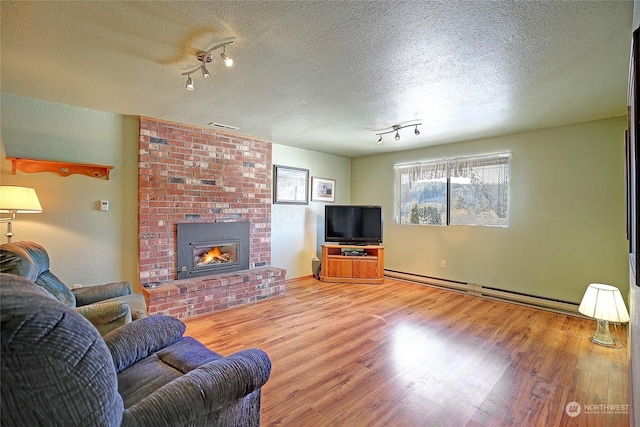 living room featuring a brick fireplace, wood-type flooring, a textured ceiling, and a baseboard heating unit