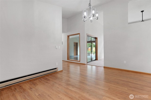 unfurnished room featuring baseboards, baseboard heating, an inviting chandelier, light wood-style floors, and a towering ceiling