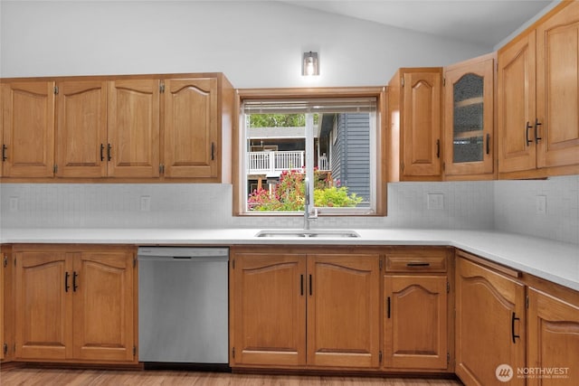 kitchen with a sink, vaulted ceiling, light countertops, light wood-style floors, and dishwasher