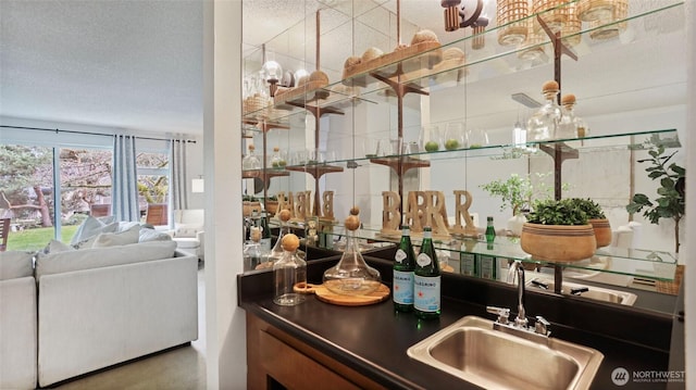 bar featuring a textured ceiling, indoor wet bar, and a sink