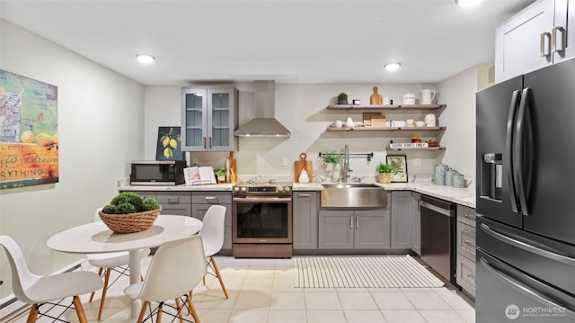 kitchen featuring a sink, light countertops, appliances with stainless steel finishes, wall chimney range hood, and gray cabinets