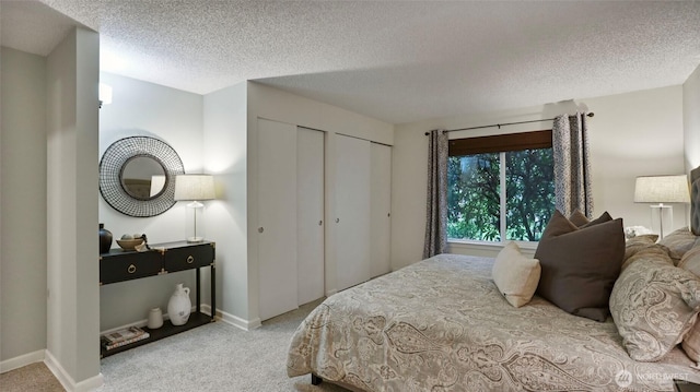 bedroom with a textured ceiling, baseboards, two closets, and light colored carpet