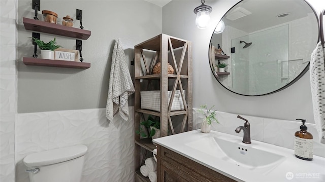 bathroom featuring tile walls, tiled shower, vanity, and toilet