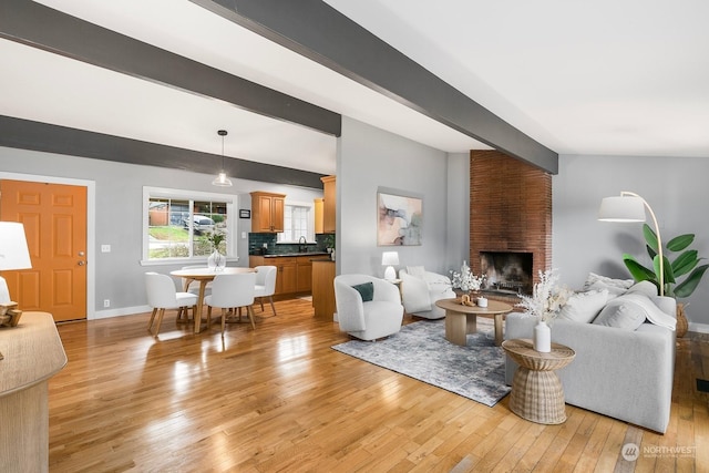 living room featuring a fireplace, sink, light hardwood / wood-style floors, and vaulted ceiling with beams