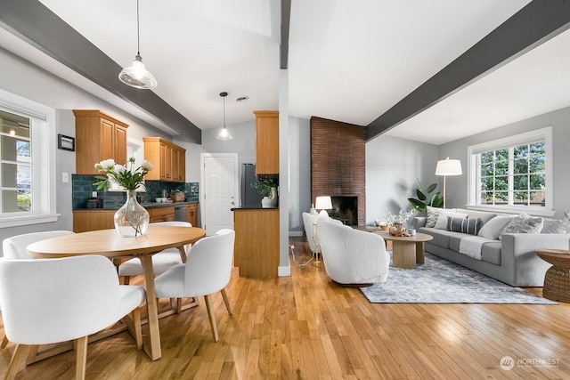 dining space featuring a fireplace, light hardwood / wood-style flooring, and vaulted ceiling with beams