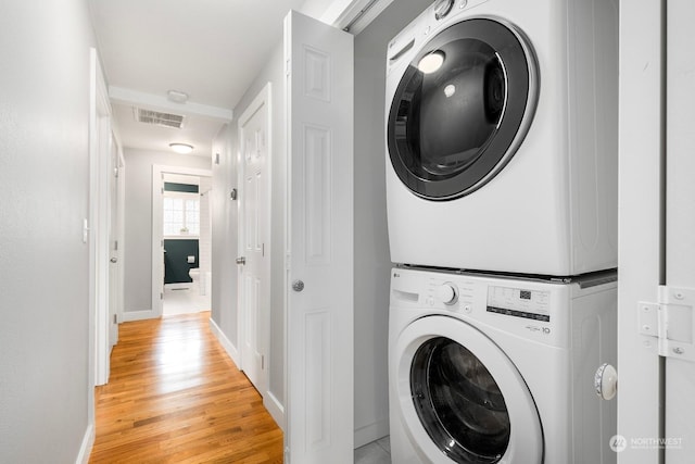 laundry area featuring stacked washer / drying machine and light hardwood / wood-style floors