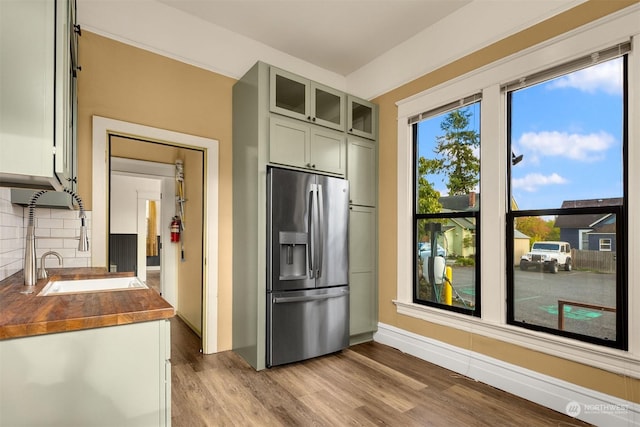 kitchen with sink, stainless steel fridge, backsplash, green cabinetry, and light wood-type flooring