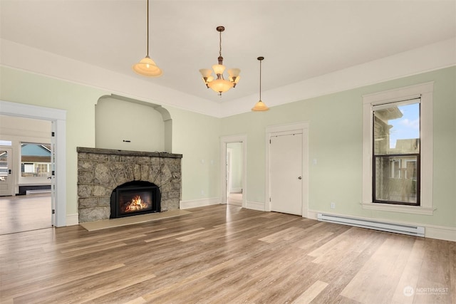 unfurnished living room with hardwood / wood-style flooring, a healthy amount of sunlight, a stone fireplace, and a baseboard heating unit