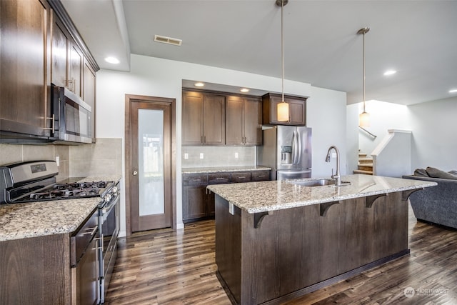 kitchen featuring sink, dark hardwood / wood-style flooring, pendant lighting, stainless steel appliances, and light stone countertops