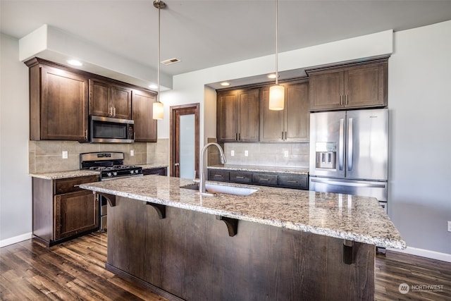 kitchen with appliances with stainless steel finishes, sink, pendant lighting, and light stone counters