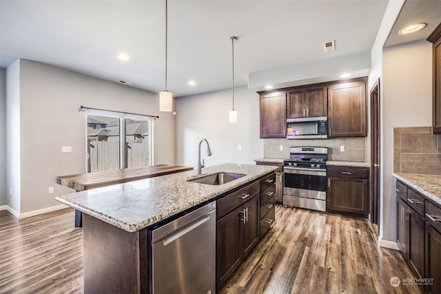 kitchen featuring sink, appliances with stainless steel finishes, a kitchen island with sink, hanging light fixtures, and dark brown cabinets