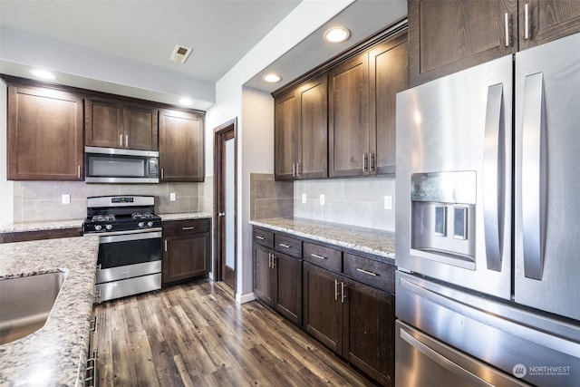 kitchen featuring light stone counters, dark brown cabinetry, dark hardwood / wood-style floors, and appliances with stainless steel finishes