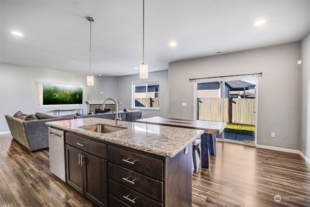 kitchen with sink, dark brown cabinets, light stone counters, a center island with sink, and decorative light fixtures