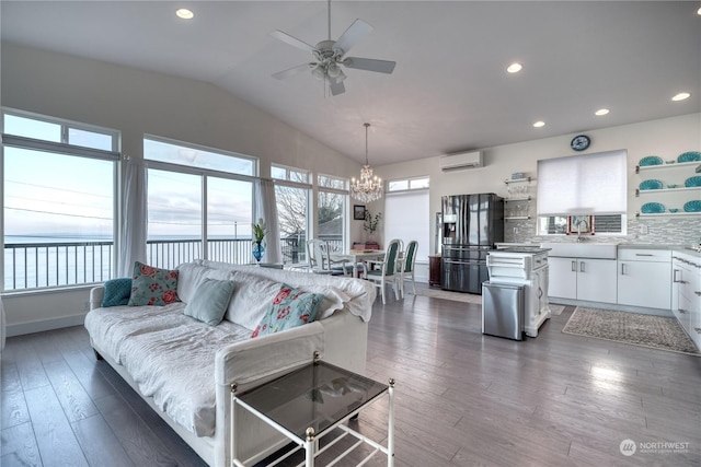 living room featuring a water view, vaulted ceiling, an AC wall unit, dark hardwood / wood-style floors, and ceiling fan with notable chandelier