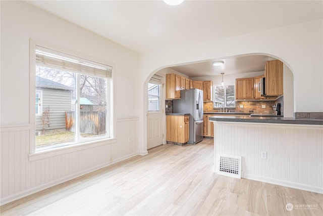 kitchen featuring stainless steel refrigerator with ice dispenser, tasteful backsplash, hanging light fixtures, light wood-type flooring, and kitchen peninsula