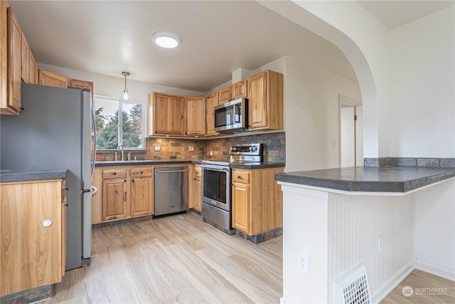 kitchen featuring appliances with stainless steel finishes, decorative backsplash, hanging light fixtures, kitchen peninsula, and light wood-type flooring