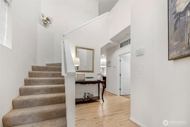 stairs with a towering ceiling, baseboards, visible vents, and wood finished floors